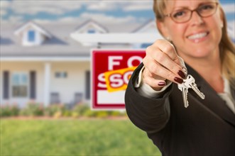 Real estate agent handing over new house keys with sold sign behind