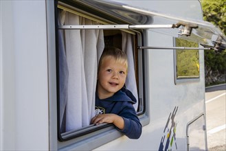 Happy small boy looking through the RV's window parked along the road