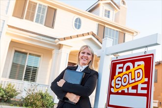 Female real estate agent in front of sold for sale sign and beautiful house