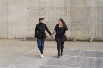 Latin lesbian couple looking at each other with affection walking hand in hand in the street. Copy space