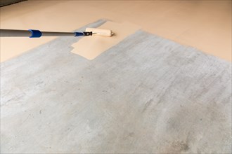 Worker painting floor of garage with roller