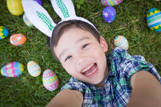 mixed-race chinese and caucasian boy outside wearing rabbit ears playing with easter eggs