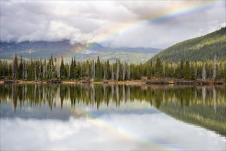 Rainbow and landscape with forest reflected in the lake