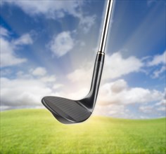 Black golf club wedge iron against grass and blue sky background