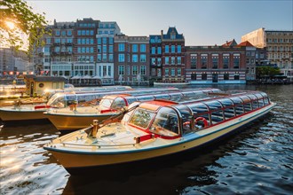Tourist boats moored in Amsterdam canal pier on sunset. Amsterdam