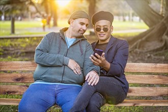 Gay Latino male couple sitting on a bench in a park at sunset