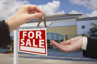 Real estate agent handing over the keys in front of vacant business office and for sale sign