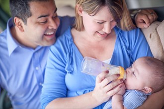 Happy attractive mixed-race couple bottle feeding their son