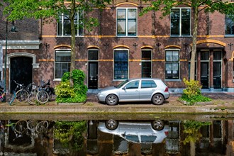Cars and bicycles parked along the canal in street of Delft with reflection