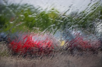 Blick durch eine nasse Windschutzscheibe auf geparkte Autos am Parkplatz