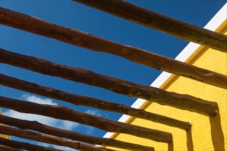 Abstract wood post beams and bright yellow wall against blue sky