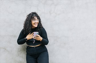 Young latin woman happy with her cell phone leaning against a wall. A young latin woman laughing with her cell phone leaning against a wall