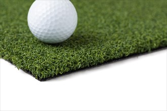 Golf ball resting on section of artificial turf grass on white background