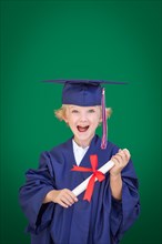 Cute young caucasian boy wearing graduation cap and gown against blank green background