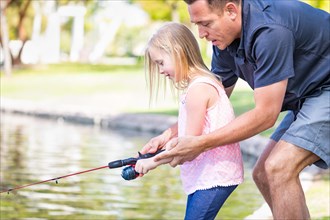Young caucasian father and daughter having fun fishing at the lake
