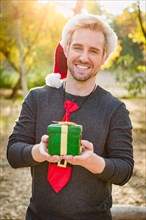 Handsome festive young caucasian man holding christmas gift outdoors
