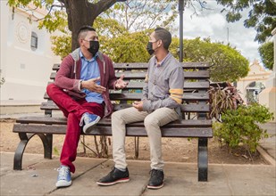 Two men with masks talking on a bench