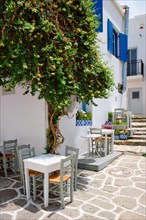 Picturesque narrow street with traditional whitewashed houses with cafe tables of Naousa town in famous tourist attraction Paros island