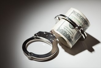 Handcuffs locked on roll of one hundred dollar bills under spotlight