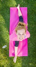 Overhead of young fit flexible adult woman outdoors on the grass with yoga mat doing the splits