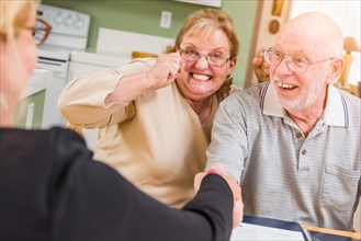 Senior adult couple celebrating over documents in their home with agent at signing
