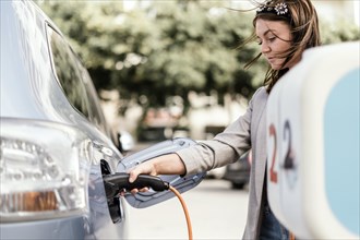 A young woman charging an electric car in urban settings