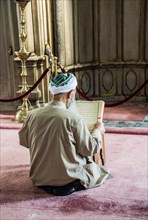 Old man reading Quran in a mosque on display