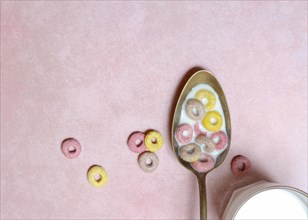Fruit-flavoured cereal rings in spoon and glass of milk