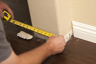 Contractor measuring for new baseboard with bull nose corners and new laminate flooring abstract