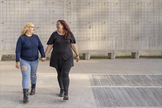 Latin lesbian couple looking at each other with affection walking hand in hand in the street