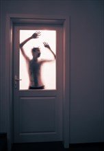 Gruselige Silhouette eines jungen Erwachsenen im Gegenlicht hinter einer verschlossenen Glastuere