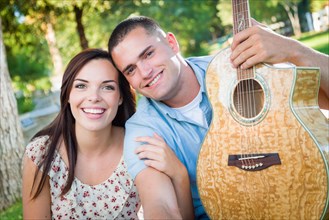 Young adult couple portrait with guitar in the park
