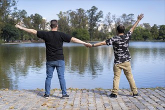 A mature white men couple holding hands and facing a lake