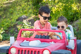 Young mixed-race chinese and caucasian brothers wearing sunglasses playing in toy car