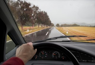 Blick durch eine nasse Windschutzscheibe eines fahrenden Auto auf die Srasse bei Regenwetter