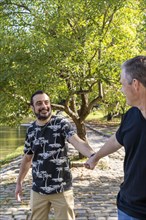 Gay man surprised and happy because his boyfriend holds his hand in public while they are walking in a lake. Coming out concept