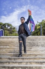 Lating gay male whit make-up on wearing fashionable hat holding lgbt flag. Concept of freedom and tolerance