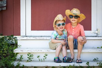 mixed-race chinese and caucasian young brothers having fun wearing sunglasses and cowboy hats