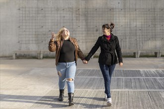 Latin lesbian couple looking at each other with affection walking hand in hand in the street