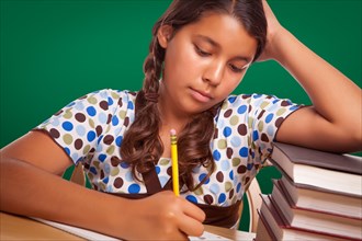 Hispanic girl student with pencil and books studying with chalk board behind
