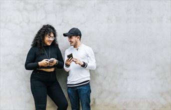 Two smiling friends checking their cell phones
