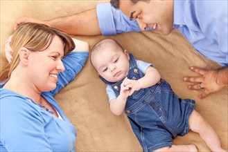 Young mixed-race couple laying with their infant on A blanket