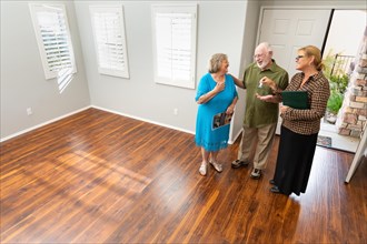 Female real estate agent handing new house keys to senior adult couple in new home