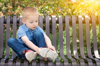 Young boy sitting on A bench putting on his shoes at the park