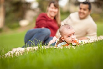Happy crawling baby boy and mixed-race parents playing in the park