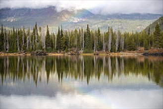 Rainbow and landscape with forest reflected in the lake