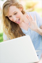 Young adult woman live video chatting outdoors using her laptop