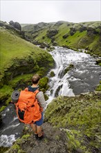 Hiker with large backpack in front of waterfall