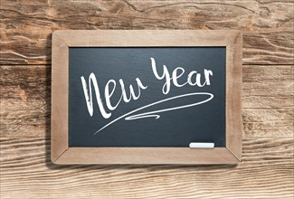 New year written on slate chalk board against aged wood background