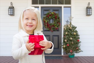 Cute young girl with gift on porch of house with christmas decorations